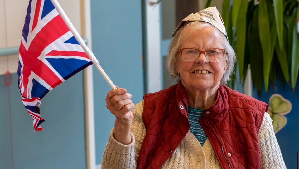Blind veteran Nancy holding a Union flag and wearing a homemade paper hat.