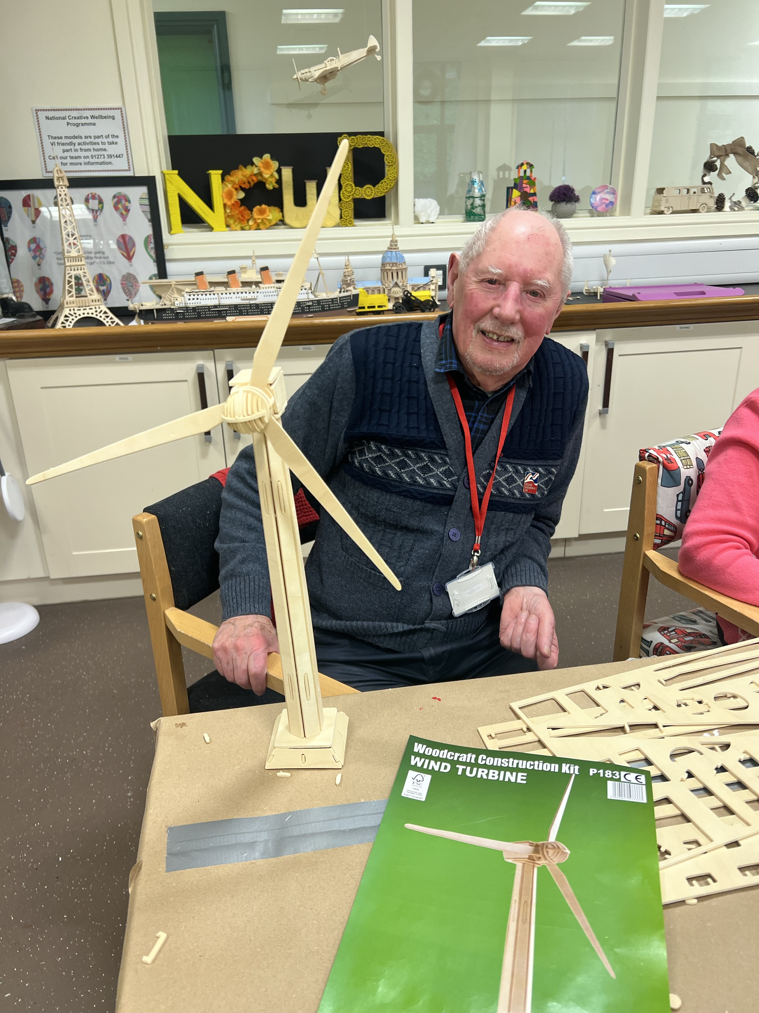 Rob sits at a table behind a wooden model of a wind turbine