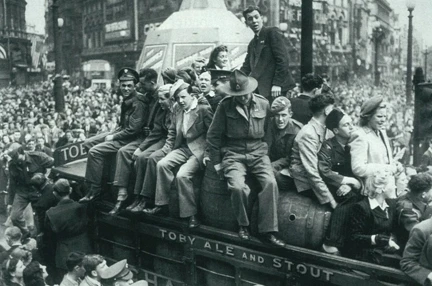 A black and white image showing the huge crowds celebrating at Piccadilly Circus. At the forefront is a group sat on top of a bus