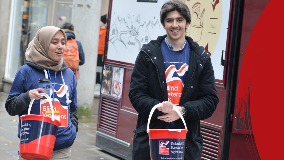 Two supporters outside holding collection buckets beside a banner with the words 'Do it for veterans'