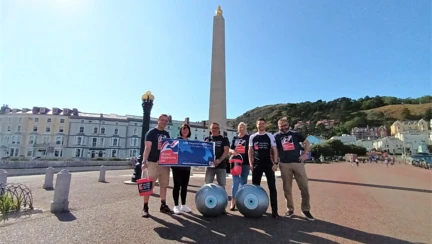 A group of six people wearing Blind Veteran UK t-shirts and stood with two large inflatable eye balls