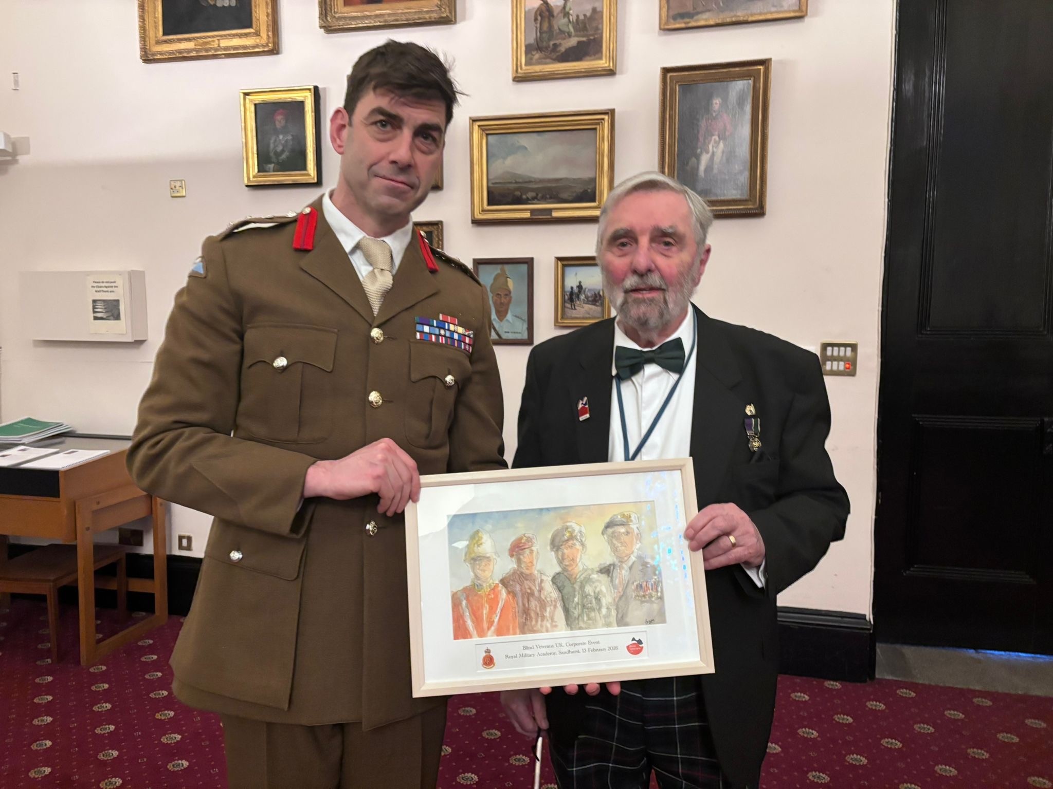 Blind veteran Bryan presenting his framed watercolour artwork depicting four military figures to a Brigadier in uniform at RMA Sandhurst
