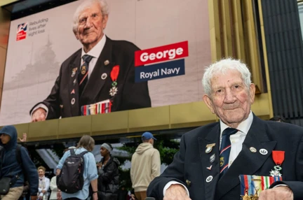 Blind D-Day veteran George sitting in front of the London billboard showing his portrait