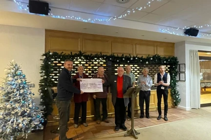 A giant cheque being held by two people with a small group in the background clapping