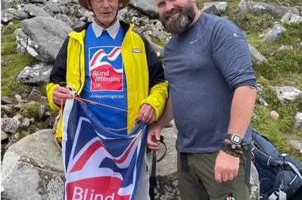 Volunteer Chris and blind veteran Pete pictured at the highest point reached on Ben Nevis, waving a Blind Veterans UK flag
