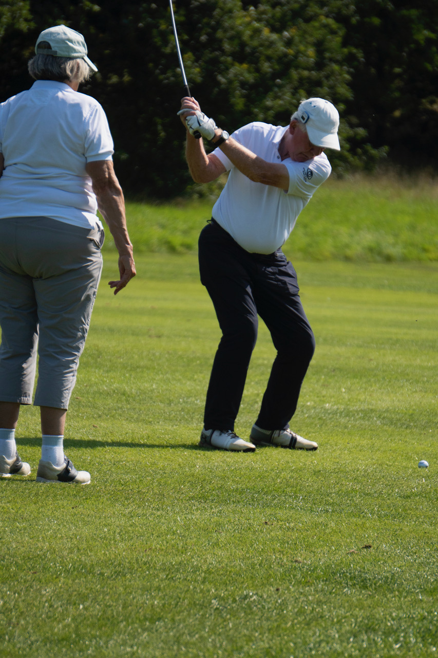 Danny mid swing with his golf club while his wife stands nearby as his guide