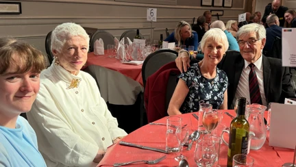 Guests are seated at a round table, smiling.