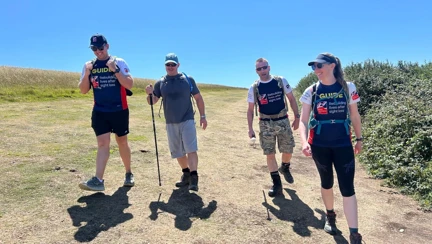 A group of four walk along the South Downs Way. Theresa and Rich are both wearing Blind Veterans UK T-shirts with 'Guide' written on the front and Stuart and Charlie walk with their white canes