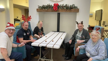 A group of people wearing reindeer antlers sit around a white table with reindeer toys