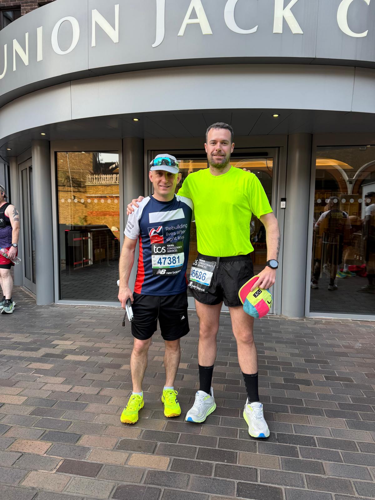 Alan in his Blind Veterans UK running vest stands outside of the Union Jack Club with his guide runner