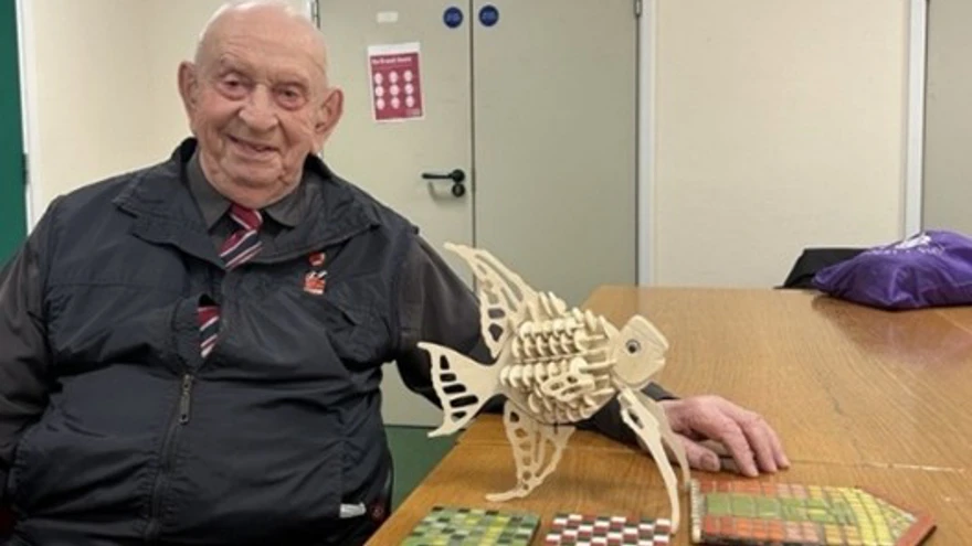 Glynne sat next to his creative projects – A wooden model of an angelfish, surrounded by colourful mosaics