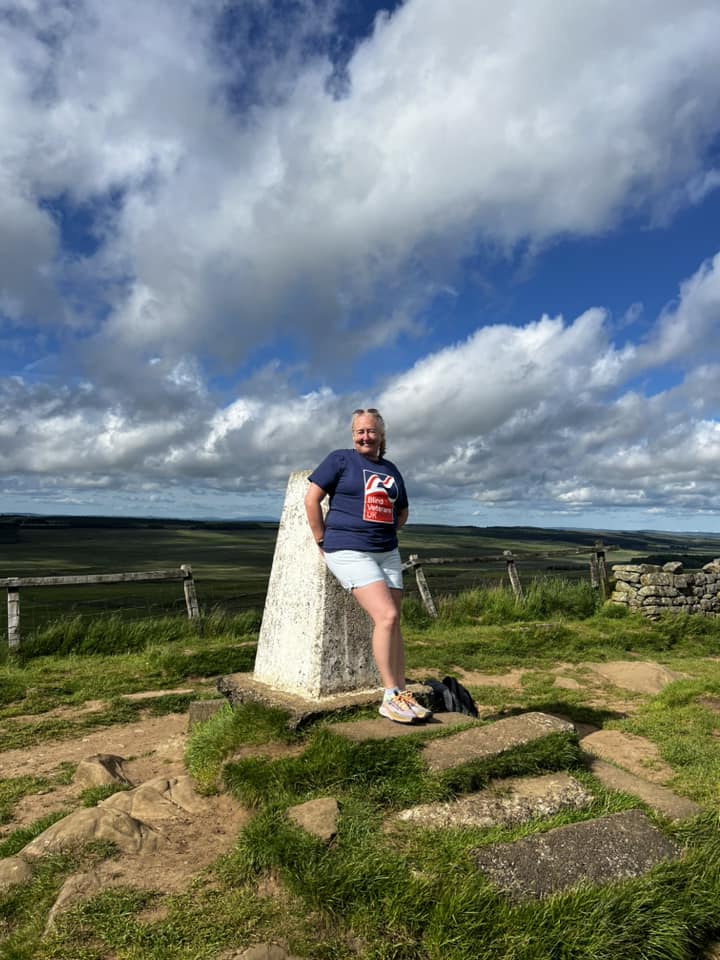 Janine is leaning against a marker point on the trail. She is smiling and wearing her Blind Veterans UK t-shirt