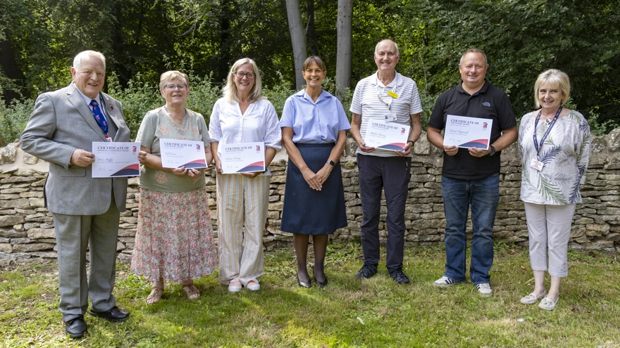 A group photographs of volunteers gathered together outside, smiling as they hold up their certificates.