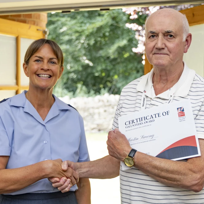 Volunteer Martin shaking hands with WO Tracey while holding his Founders Award certificate at RAF Cranwell.