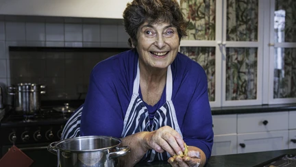 Penny leaning on her kitchen sideboard smiling and looking at the camera. Her oven behind her and a bowl beside her on the left and a baking tray on the right.