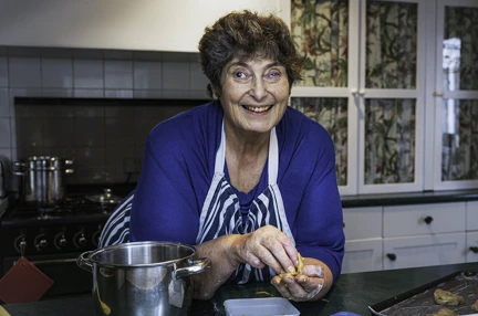 Penny leaning on her kitchen sideboard smiling and looking at the camera. Her oven behind her and a bowl beside her on the left and a baking tray on the right.