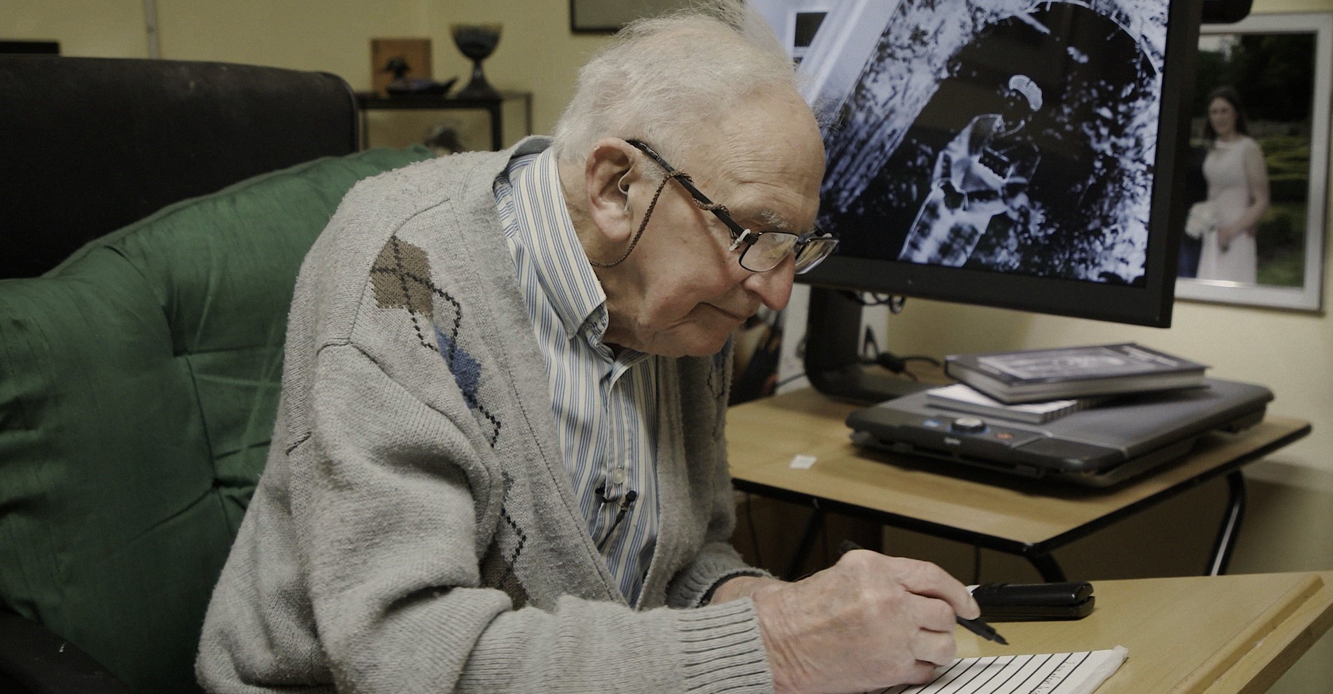 Blind veteran John, sitting at a desk writing on a note pad