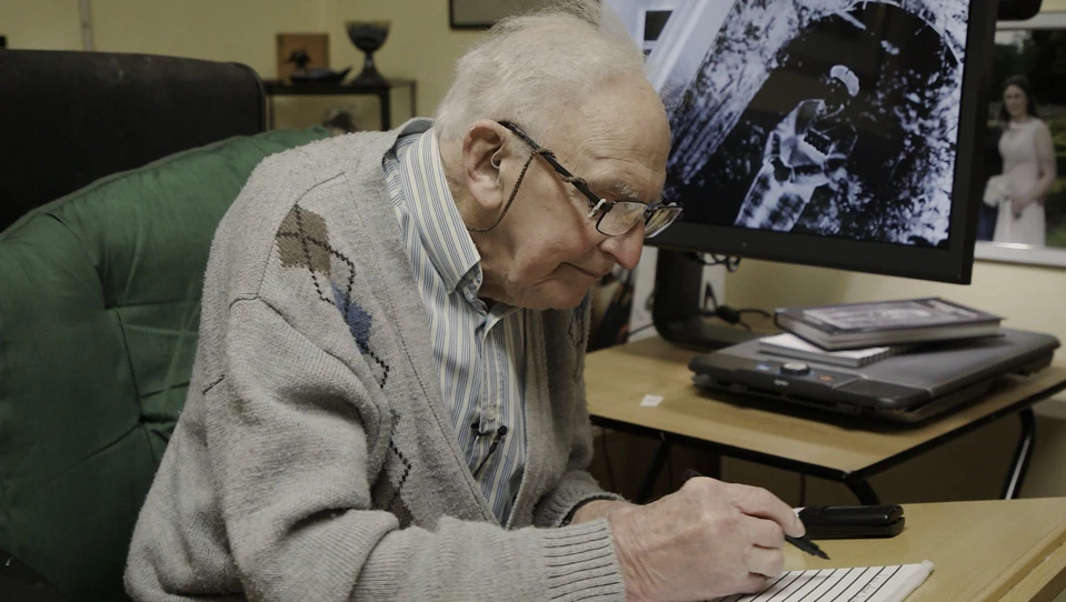 Blind veteran John, sitting at a desk writing on a note pad