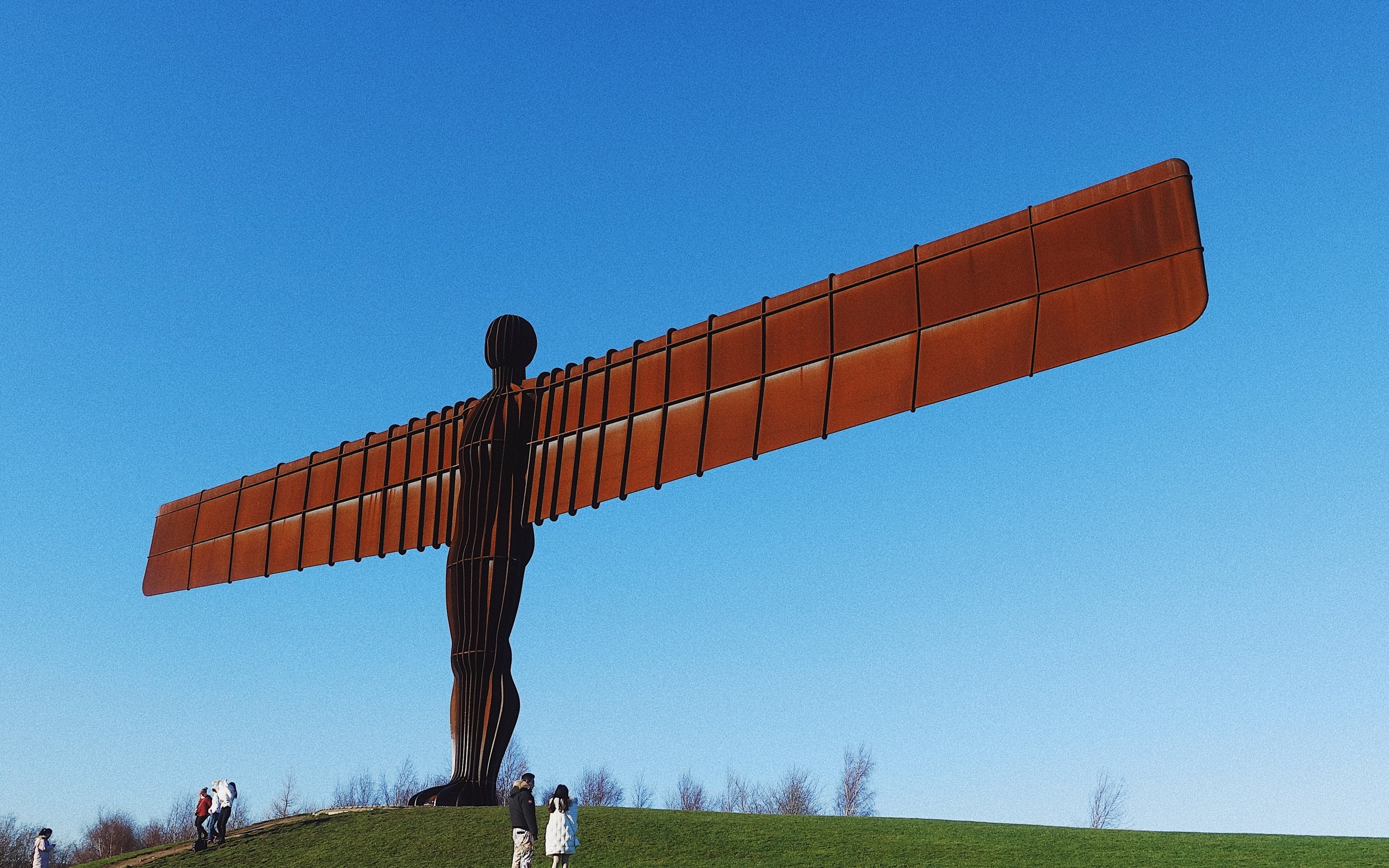 The Angel of the North statue, a large steel sculpture with wide spanning wings, placed on a grassy hill.