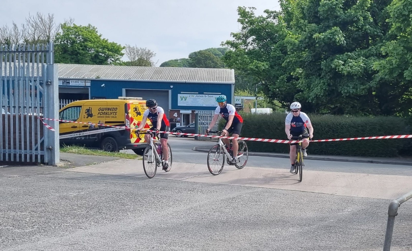 The three cyclists just a metre away from the finish line tied across the gates at their place of work