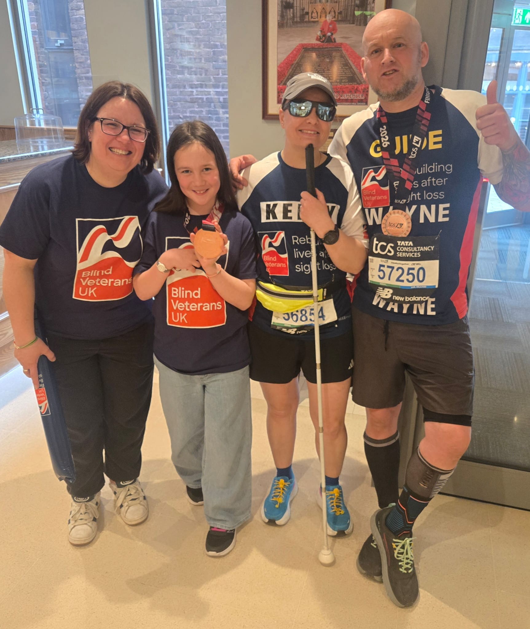 Kelly is posing for a picture with her wife and daughter and her guide Wayne following the marathon. 