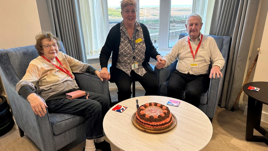 Terry, Joyce and Lesley are sat behind a cake that was baked to welcome the couple back to Rustington