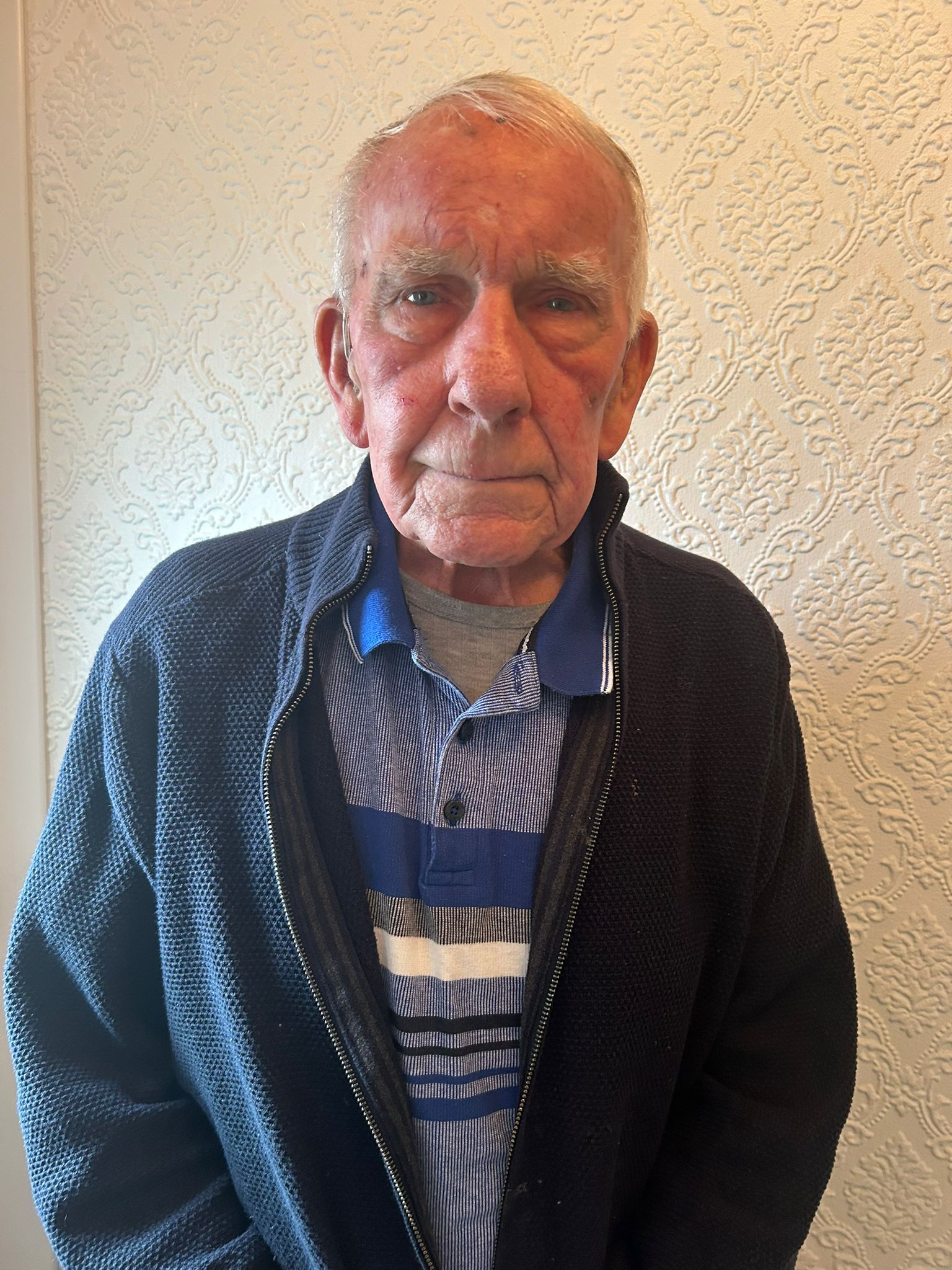 Alan wearing a stripy blue t-shirt and a navy blue jacket looks straight at the camera for his picture