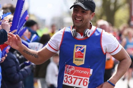 Charity supporter Dominic smiling as he runs along a crowd, wearing a Blind Veterans UK vest and holding his hand out to wave as he passes