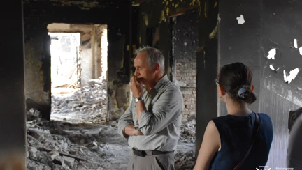 Nick Caplin is pictured with his hand to his mouth, looking pensive as he stands in a destroyed building in Ukraine