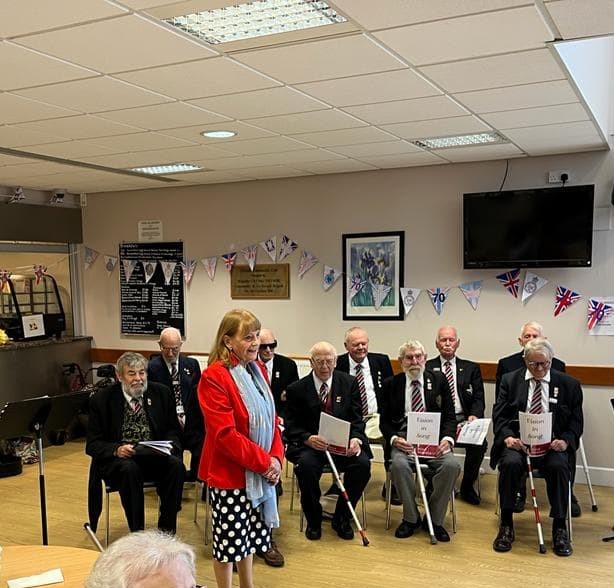 Jennie stands in the foreground in formal attire, with the choir sitting down behind her, also in formal attire, ready to perform