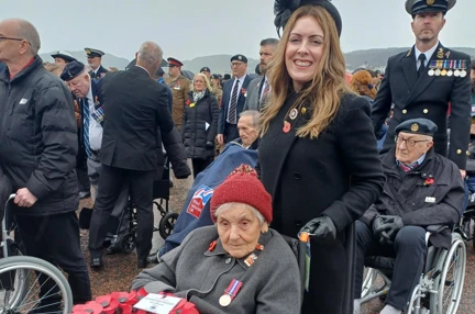 Blind veteran Mary is pushed in her wheelchair by Kelly. Mary has the wreath on her lap.