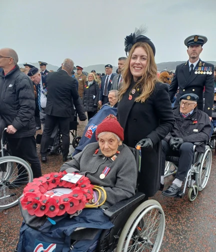 Blind veteran Mary is pushed in her wheelchair by Kelly. Mary has the wreath on her lap.