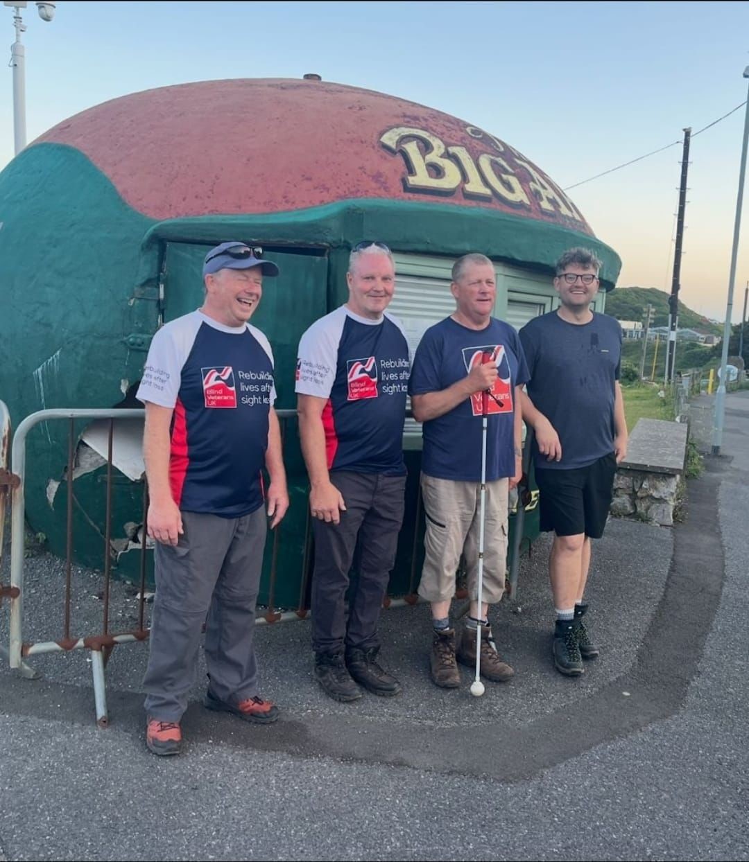 A group shot of the four men during the challenge. Stood in front of a kiosk that looks like a large apple.